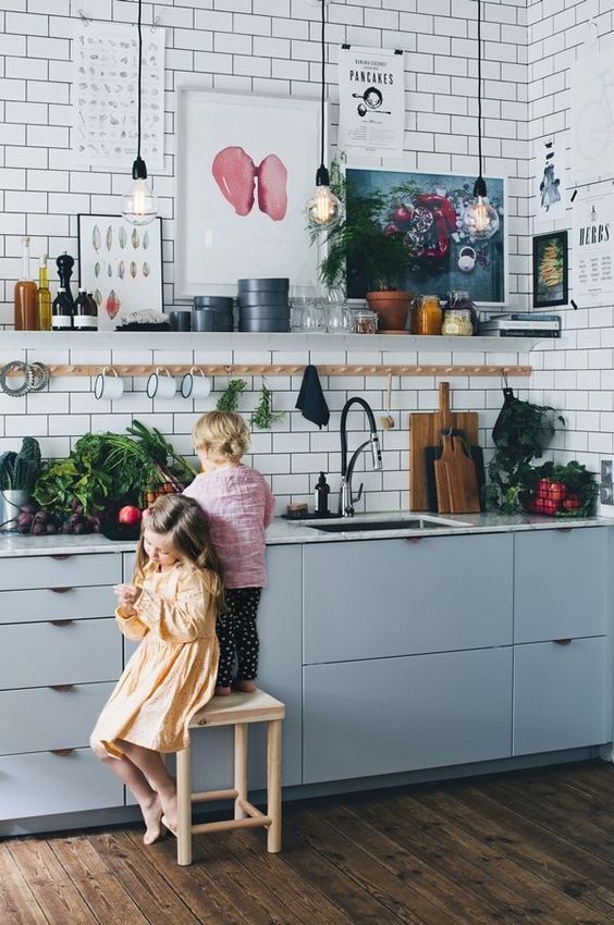 a Scandinavian kitchen with light grey cabinets and white subway tiles, pendant lamps and a shelf for storage