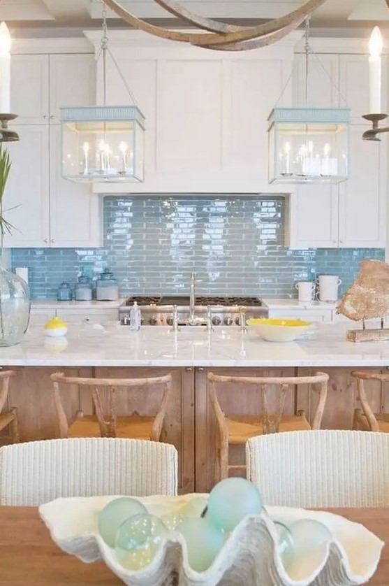 a beach cottage kitchen with white shaker cabinets, a glossy blue tile backsplash, blue and white pendant lamps and a wooden kitchen island
