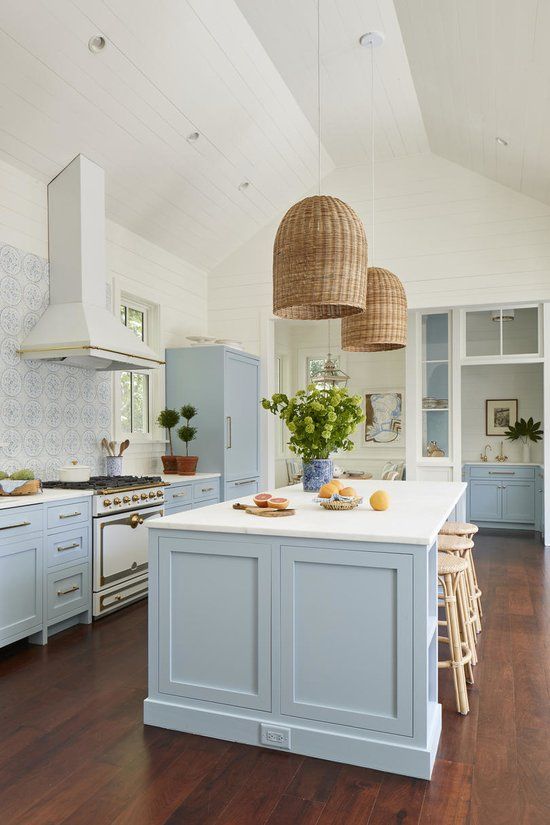a beautiful coastal kitchen in light blue and white, with a mosaic tile backsplash, wicker lampshades and rattan stools plus greenery