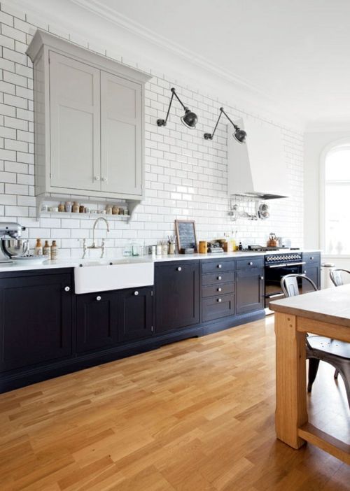 a beautiful kitchen with navy lower cabinets, a grey upper cabinet, a white hood, white subway tiles on the wall