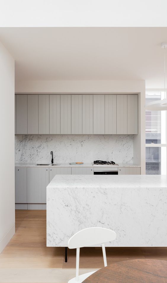 a beautiful minimalist kitchen with dove grey shiplap cabinets, a white marble backsplash and a matching kitchen island