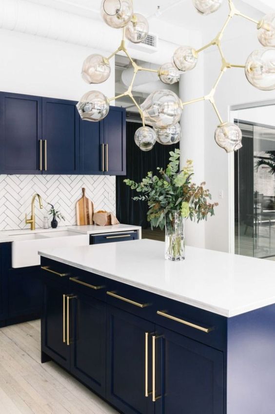 a bold and chic kitchen with navy cabinets, white countertops and a backsplash and a catchy chandelier with gold touches