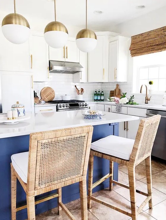 a bold coastal kitchen with white cabinets, a navy kitchen island with a white countertop, rattan chairs, woven shades and open shelves