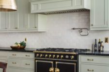 a bright art deco kitchen in pale green, with a white tile backsplash, a vintage cooker and gold touches