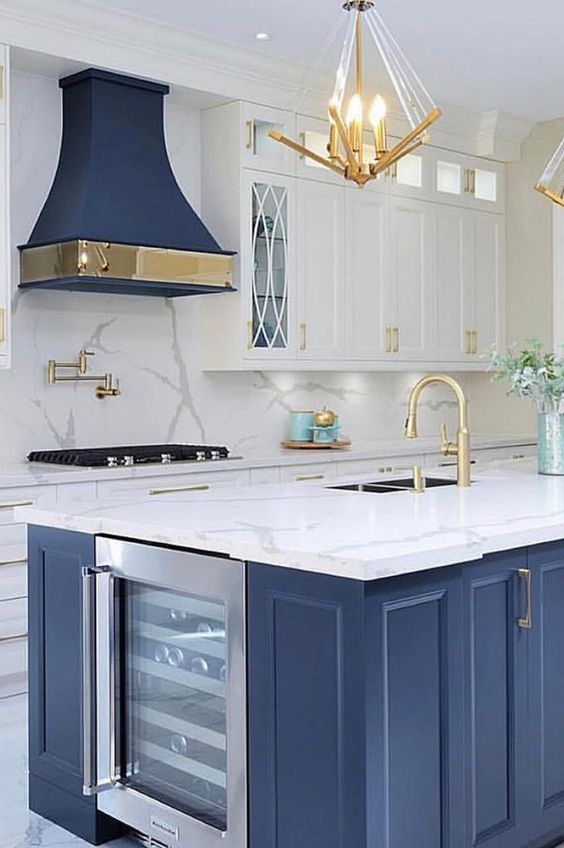 a bright kitchen with white cabinets, a blue kitchen island and hood and lots of gold to make the space exquisite