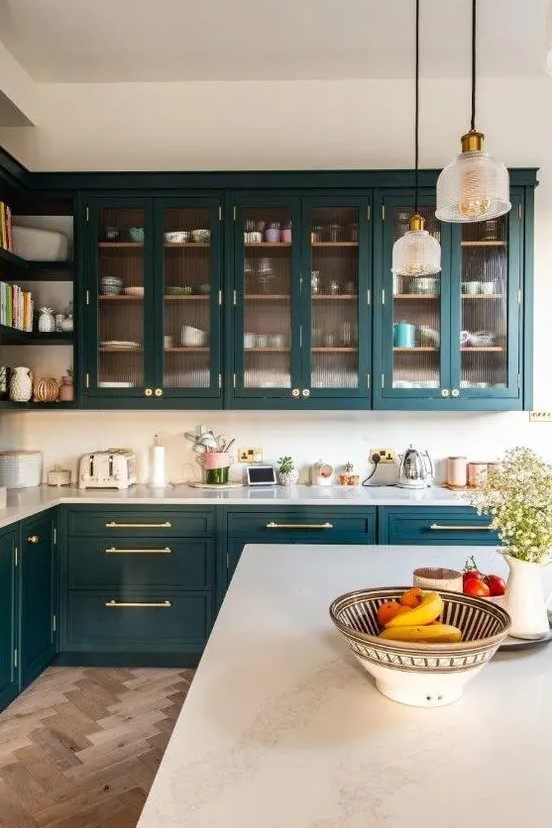 a chic and refined teal kitchen with glass and shaker cabinets, white countertops and a white backsplash plus pendant lamps