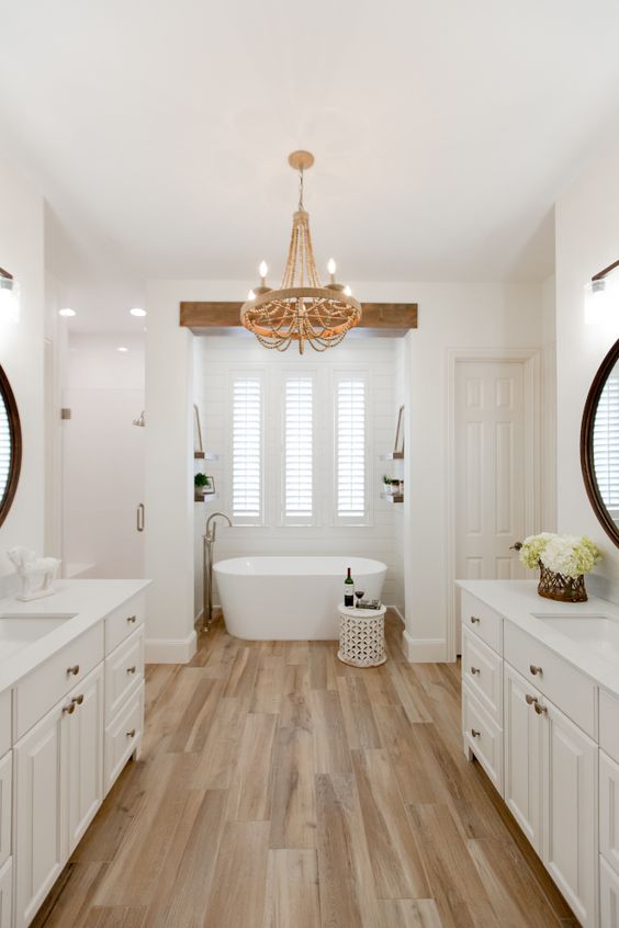 a chic bathroom with wooden tiles on the floor, a bathtub in the niche, two vanities and a chic chandelier