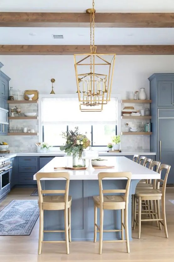 a chic coastal kitchen with ocean blue shaker cabinets, marble tiles, a large kitchen island with white countertops, wooden stools and gold pendant lamps