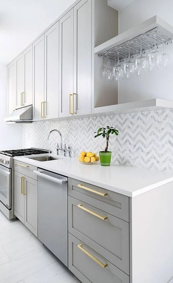 a chic grey kitchen with shaker cabinets, a chevron tile backsplash in grey and white, gold handles is stylish