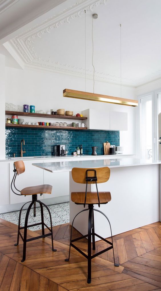 a chic kitchen with sleek white cabinets, a bold blue tile backsplash, a kitchen island, stained stools and shelves