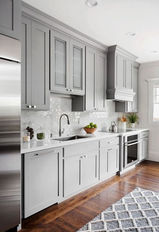 a chic light grey traditional kitchen with a white hexagon tile backsplash and a geometric rug