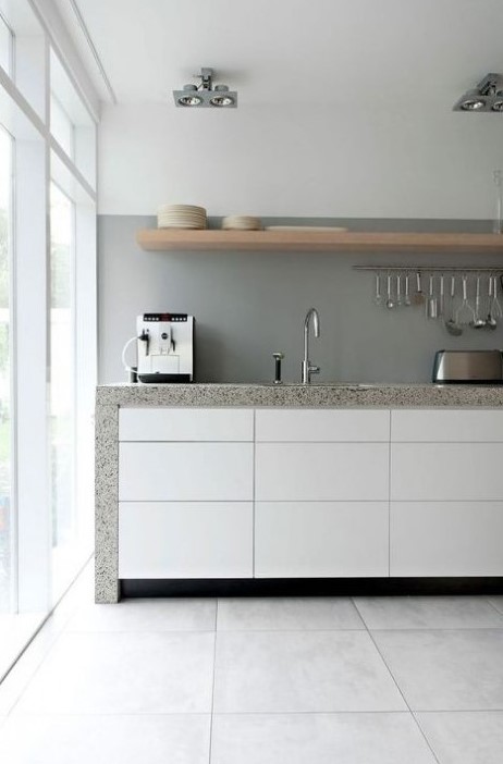 a chic minimalist kitchen with sleek white cabinets, a concrete backsplash and grey stone countertops plus a wooden shelf