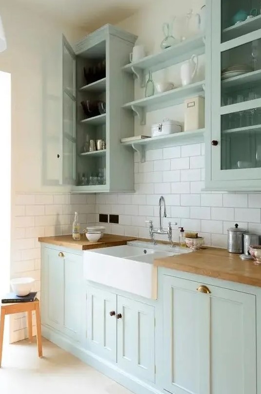 a chic mint green farmhouse kitchen with shaker style cabinets, butcherblock countertops, a white subway tile backsplash and a vintage faucet