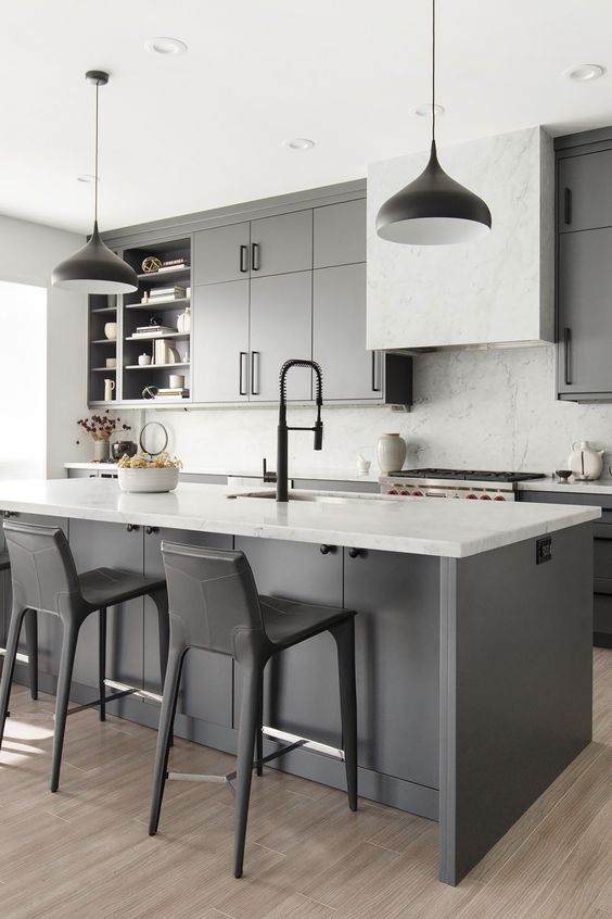 a chic modern monochromatic kitchen with grey cabinets and a kitchen island, white marble countertops and a backsplash, black pendant lamps and black stools