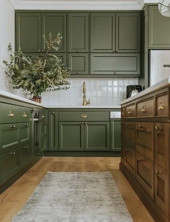 a chic olive green farmhouse kitchen with shaker cabinets, a white tile backsplash, a dark-stained kitchen island and a printed rug