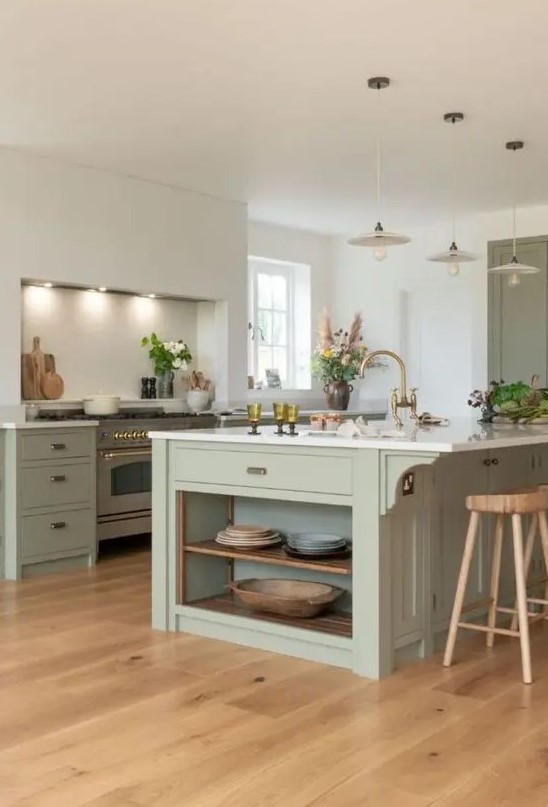 a chic sage green kitchen with a separate cooking zone, flat panel cabinets, white stone countertops, brass fixtures