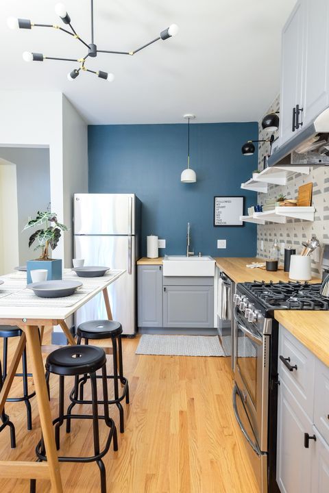 a cihc and cool kitchen with a navy accent wall, grey cabinets, butcherblock countertops, a trestle table and black stools