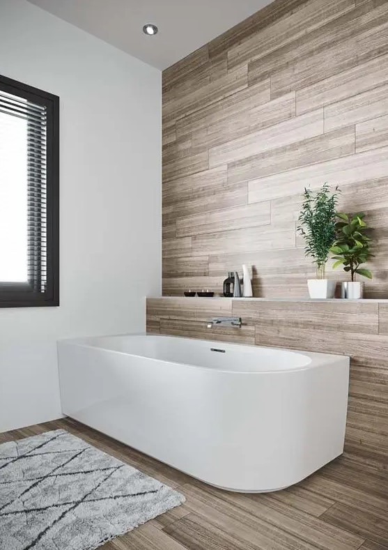 a clean contemporary bathroom done with laminate, with a chic bathtub and a raised shelf over it, with a window and a printed rug