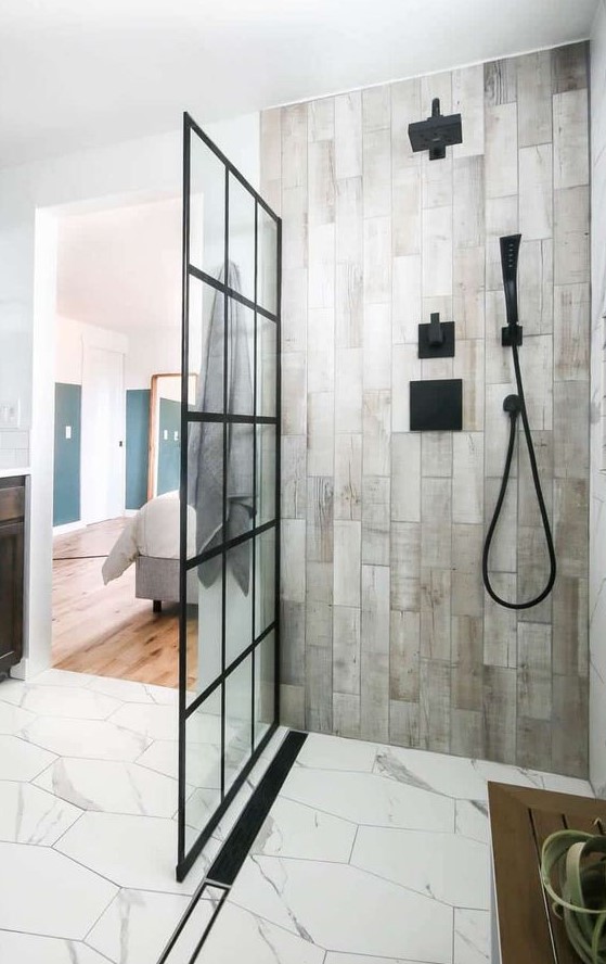 a contemporary bathroom clad with hex white stone tiles and wood look ones, with black fixtures and a glass framed wall is cool