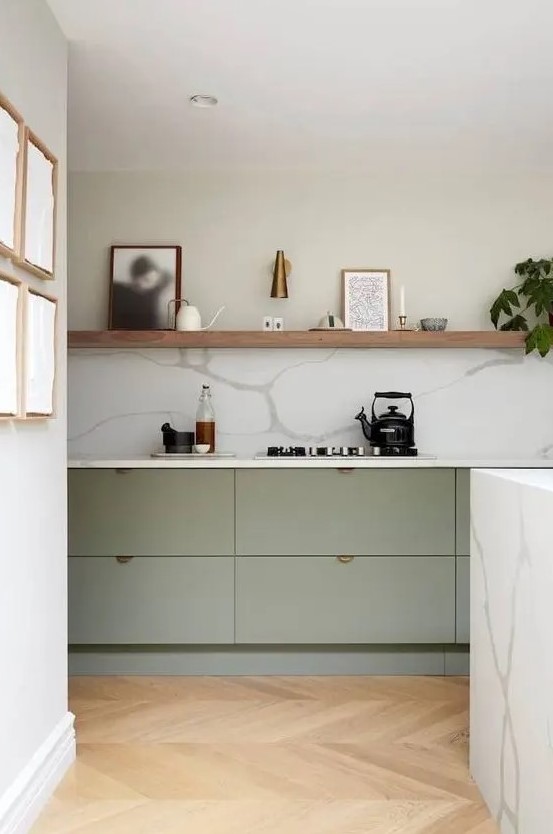 a contemporary kitchen with lower sage green cabinets and a long shelf instead of upper ones, a white marble backsplash and countertops