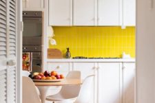 a contemporary kitchen with white cabinets, a bright yellow tile backsplash and a lamp, white chairs and neutrals