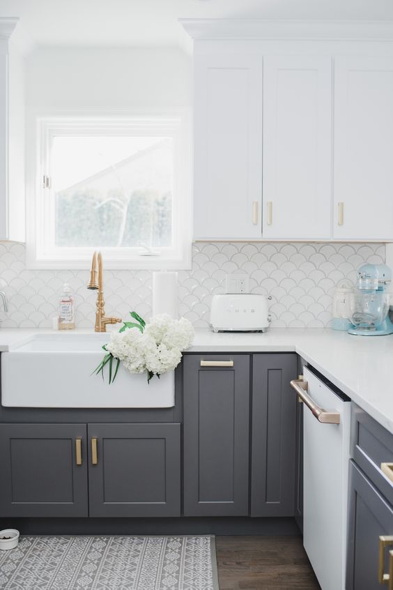a contemporary kitchen with white upper cabinets and lower grey ones, gold and brass handles plus a white fish scale backsplash