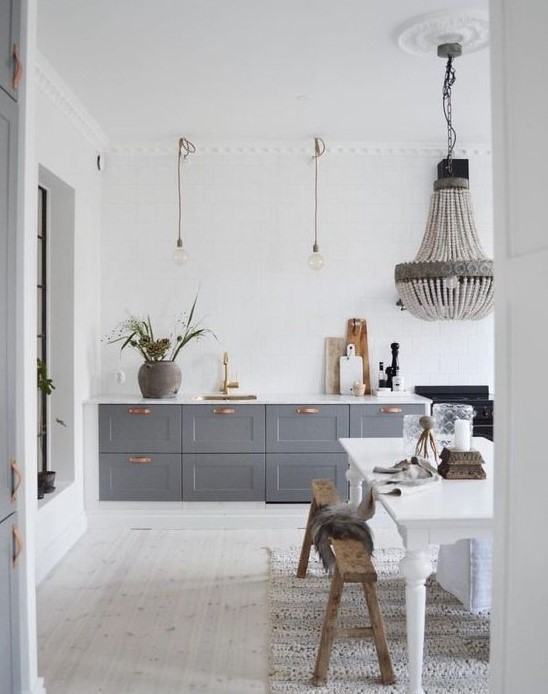 a contemporary meets vintage kitchen with grey cabinets, pendant lamps and a chandelier, a white vintage table and benches