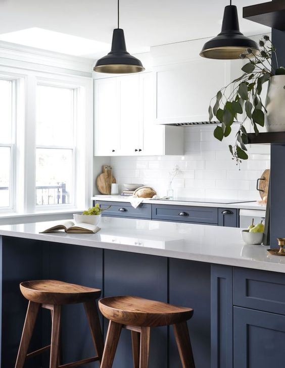 a contrasting kitchen with navy and white cabinets, a white tile backsplash, woodne stools and pendant lamps is a chic space