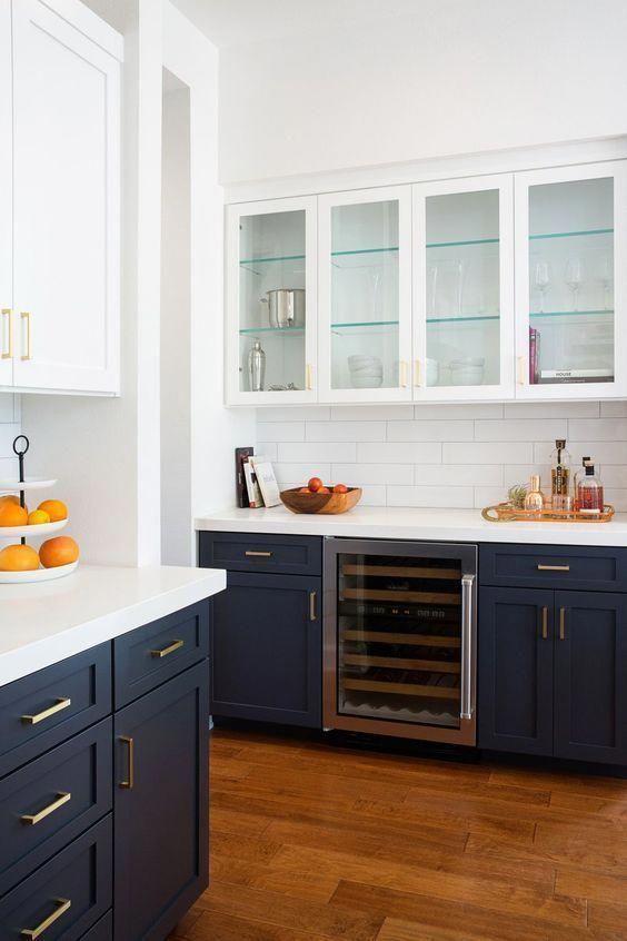a contrasting kitchen with navy lower cabinets, white upper ones, white tile backsplashes and white countertops