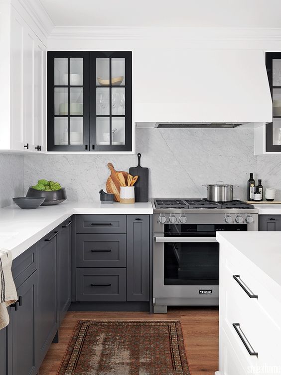 a contrasting kitchen with white upper cabients and charcoal grey ones, black glass frame cabinets and a white backsplash and countertops