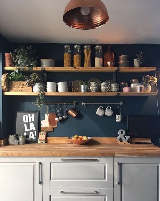 a cool farmhouse kitchen with a navy wall, a dove grey cabinet, butcherblock countertops, open shelves and potted plants