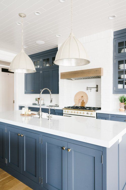 a cool kitchen with blue shaker style cabinets, white countertops and a backsplash, pendant lamps