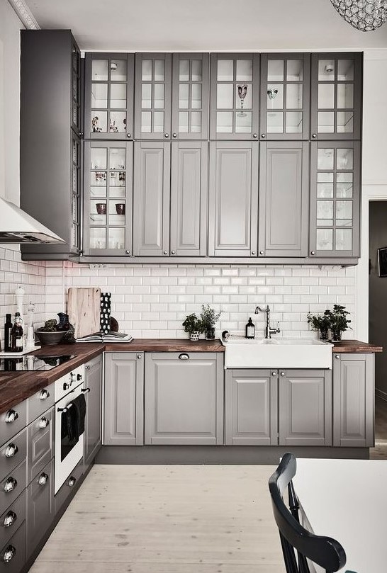 a cozy traditional grey kitchen with usual and glass cabinets, with rich-colored wooden countertops and metal knobs