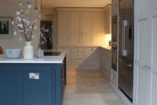a dove grey kitchen with a bold blue kitchen island, white stone countertops and a neutral tile floor