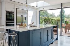 a dove grey kitchen with a large navy kitchen island and white stone countertops plus vintage stools and pendant lamps