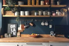 a dove grey kitchen with a navy wall, wooden shelves and butcherblock countertops plus touches of copper and greenery