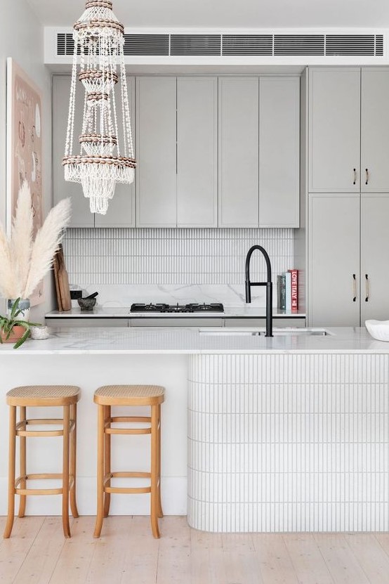 a dove grey kitchen with white skinny tiles on the backsplash and kitchen island, a macrame chandelier and wooden stools