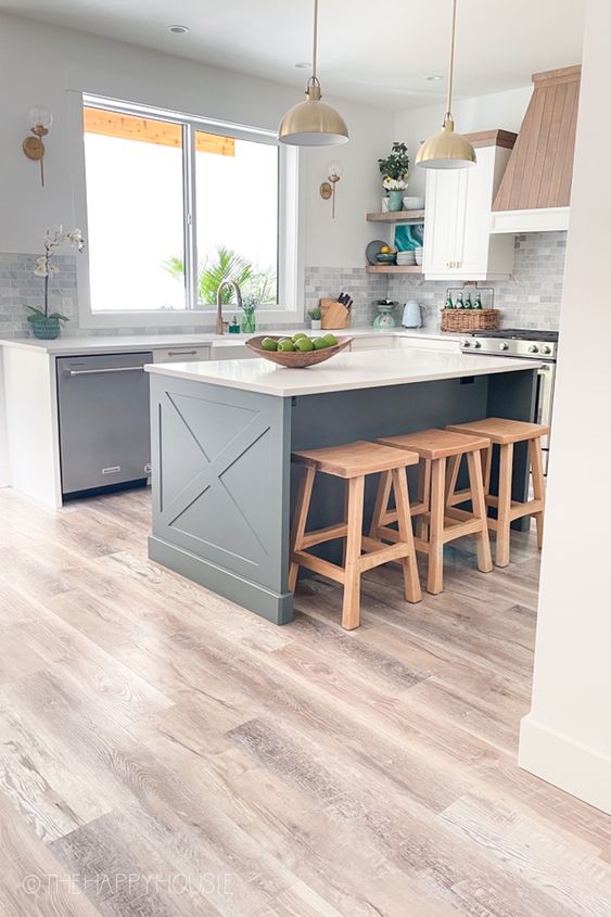 a farmhouse kitchen with charcoal grey cabinets and white ones, a wood clad hood and wooden stools, pendant lamps