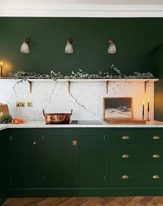 a hunter green kitchen with vintage cabinets, gold handles, an open shelf with greenery and a white stone backsplash