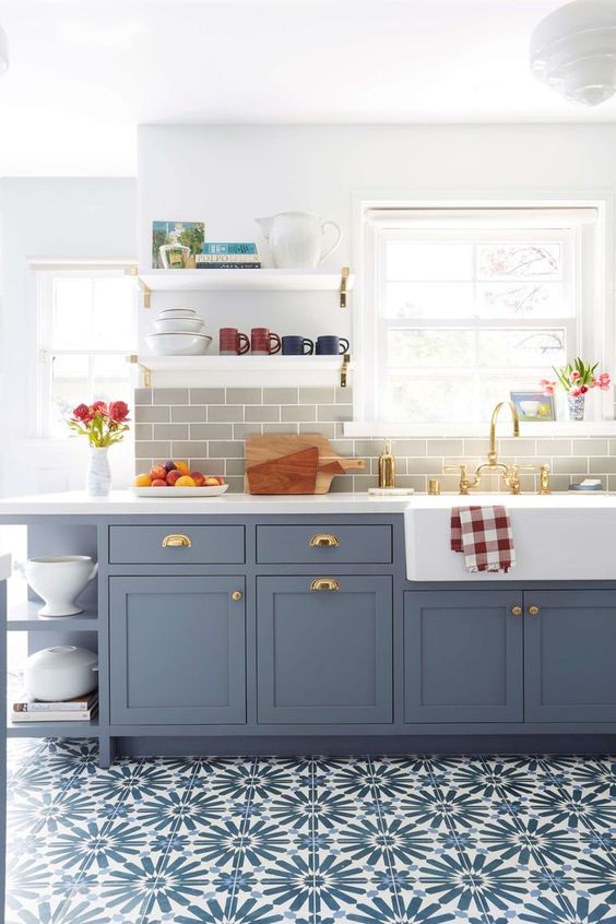a lovely and cozy kitchen with blue shaker style cabinets, a grey subway tile backsplash, a bold blue tiled floor and open shelves