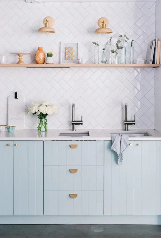 a lovely kitchen with light blue kitchen cabinets, a white tile backsplash and white countertops, an open shelf for displaying stuff