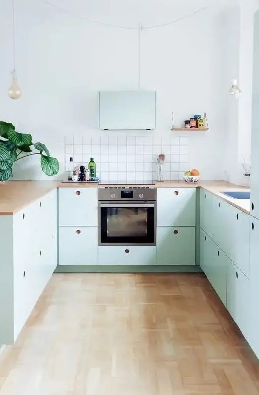 a lovely mint blue Scandinavian kitchen with plywood cabinets, butcherblock countertops, a square tile backsplash and pendant bulbs