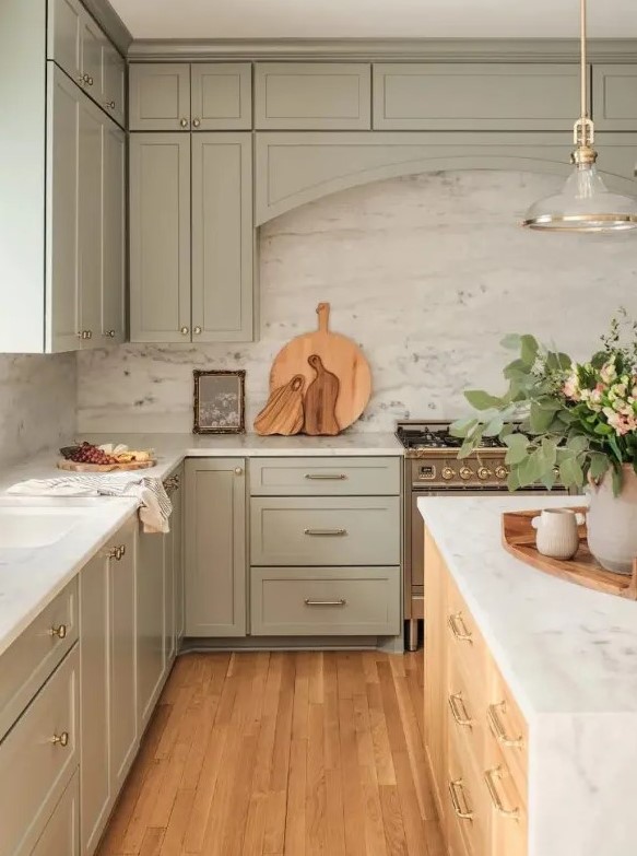 a lovely sage green kitchen with shaker cabinets, a white stone backsplash and countertops, a stained kitchen island and a chic pendant lamp