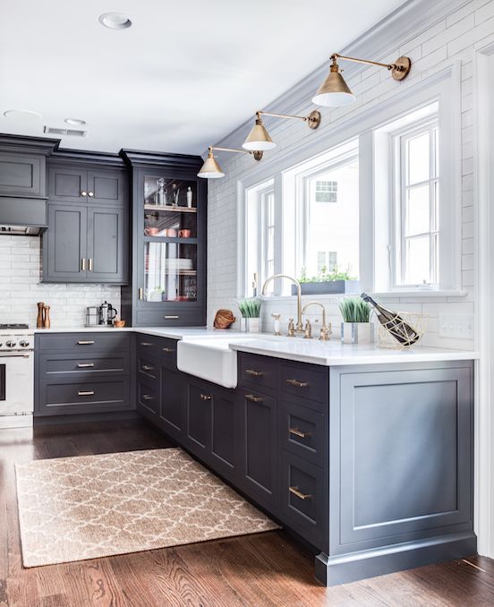 a mid-century modern kitchen with graphite grey cabinets, white countertops, brass lamps and handles plus white tiles on the backsplash