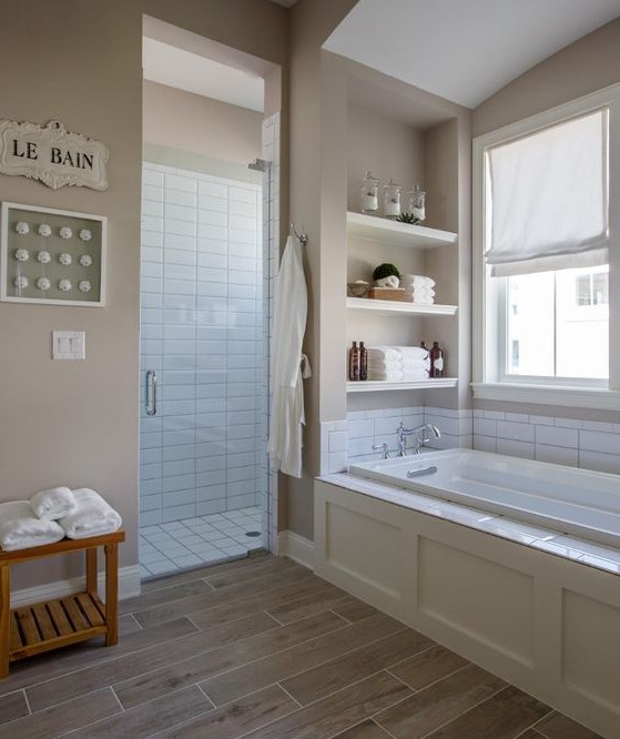 a mid-century modern tan bathroom with tan walls, wood look tiles on the floor, built-in shelves and white subway tiles