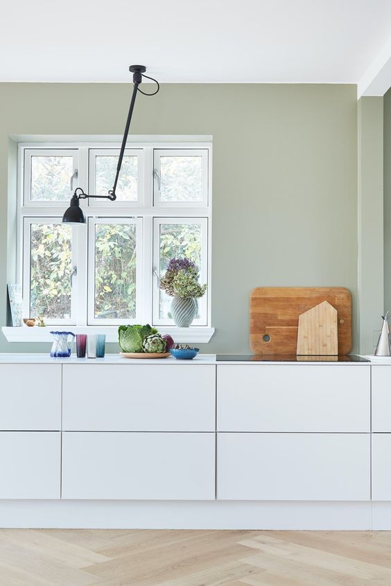 a minimal Scandinavian kitchen with pale green walls, sleek white cabinets and a black ceiling lamp is a cool and airy space