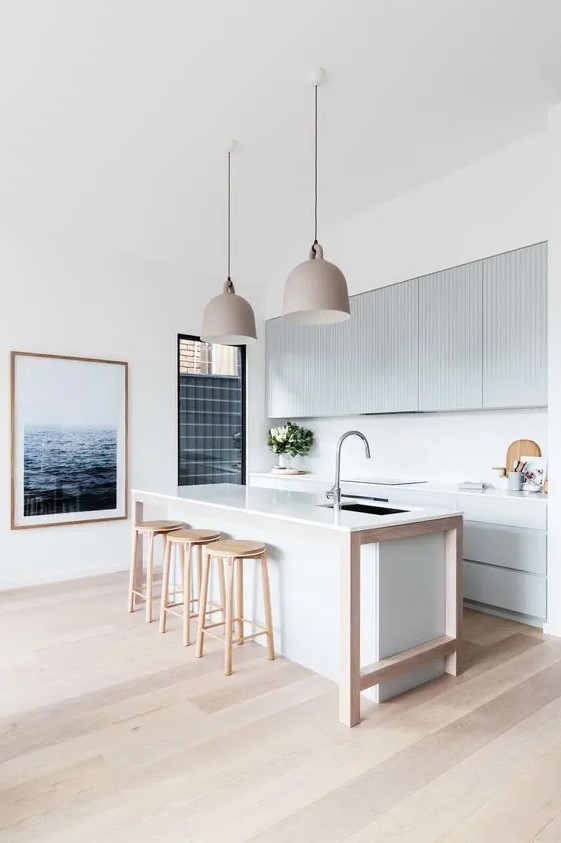 a minimalist beach kitchen with light blue ribbed cabinets and a white kitchen island, wooden stools and pretty pendant lamps