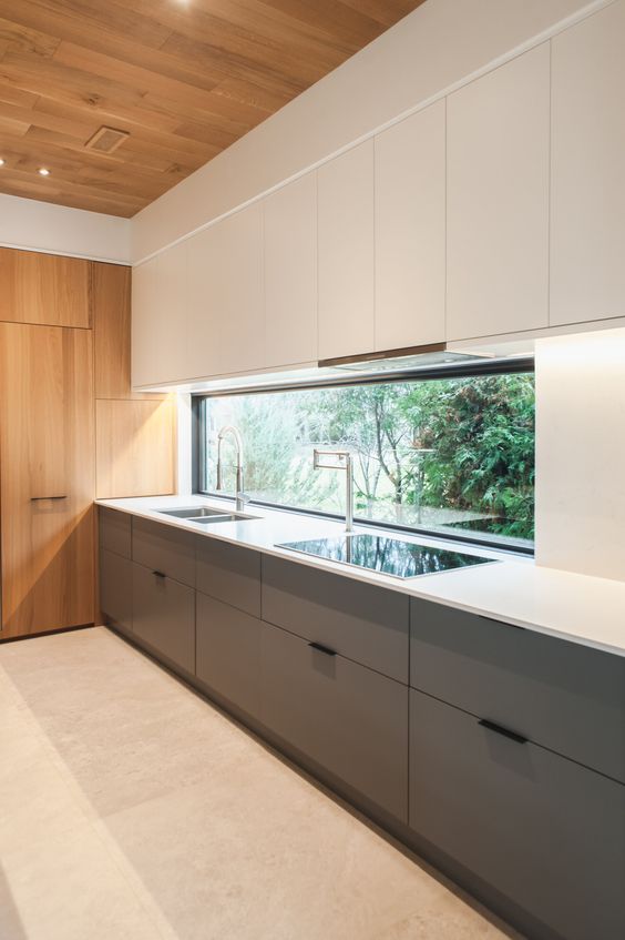 a minimalist kitchen with lower grey and upper white cabinets, a window backsplash, a white countertop and stained wood for a warmer feel