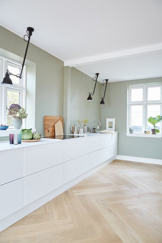 a minimalist kitchen with pale green walls, white sleek cabinets, black ceiling lamps looks fresh and natural