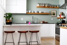 a minimalist kitchen with white cabinets, pale green walls, stone countertops and wooden shelves and stools